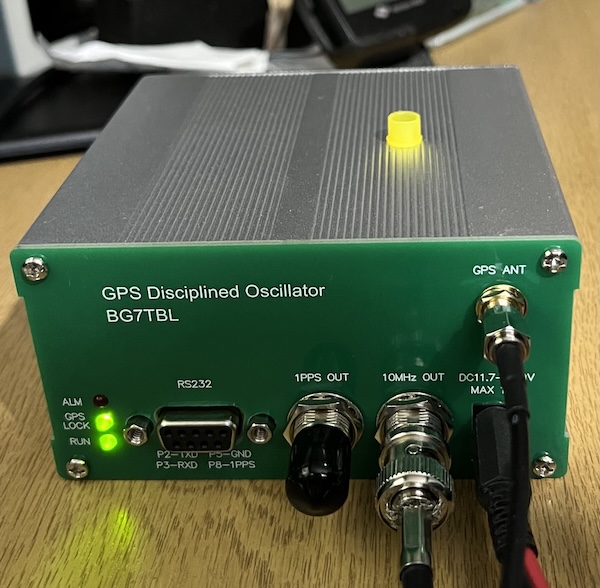 A photo of a BG7TBL GPSDO with a green facia, two BNC connectors, a D-type connector and three LEDs.