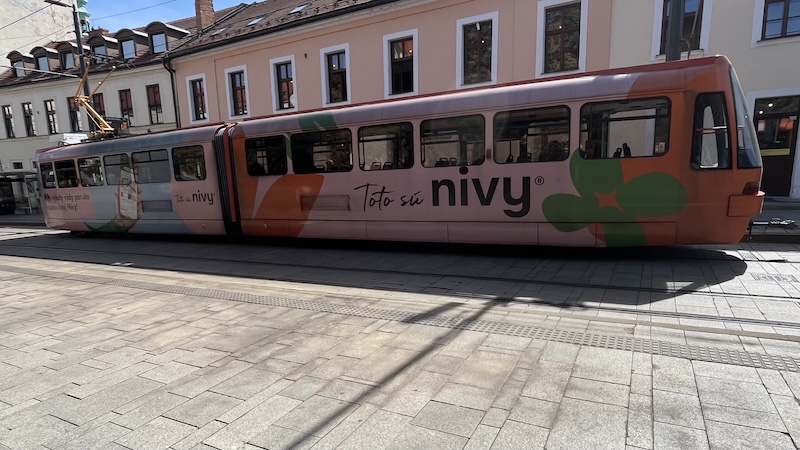 A photo of an articulated tramcar set against a building. The tram has 'Toto sú nivy' written on it plus a green and orange graphic to the right.