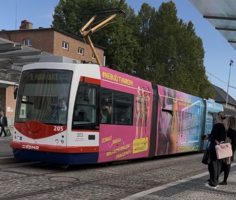 A photo of a tram, mainly a pink-ish colour with advertising.